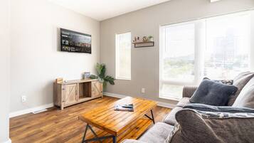 Una sala de estar con una mesa de centro de madera, un sofá gris y un mueble bajo con una planta.