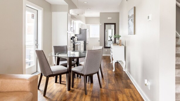 A modern kitchen with a glass dining table, grey chairs, and wooden flooring.