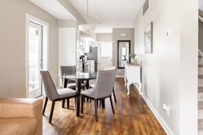 A modern kitchen with a glass dining table, grey chairs, and wooden flooring.