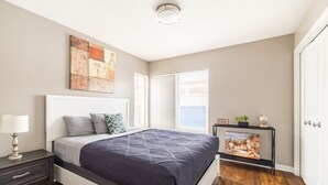 A bedroom with a bed, bedside table, lamp, artwork, and a TV on a stand.