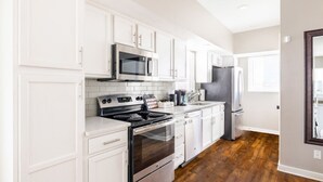 A modern kitchen with white cabinetry, stainless steel appliances, and a wooden floor.