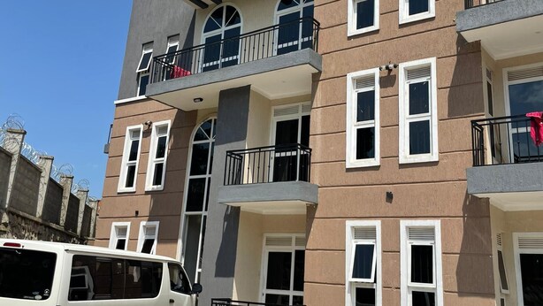 A multi-story residential building with balconies, a parking area, and a white van parked in front. - Yo House (Kampala)