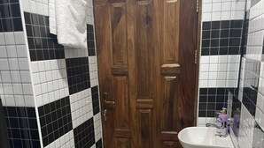 A bathroom with a wooden door, a white sink, and a toilet. - Yo House (Kampala)