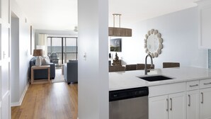 A modern kitchen with white cabinetry, a built-in dishwasher, and a large window overlooking a balcony.
