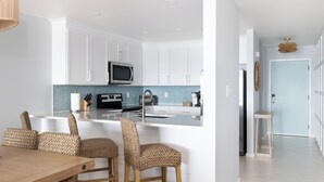 A modern kitchen with white cabinets, a central island, and a dining area with wicker chairs.