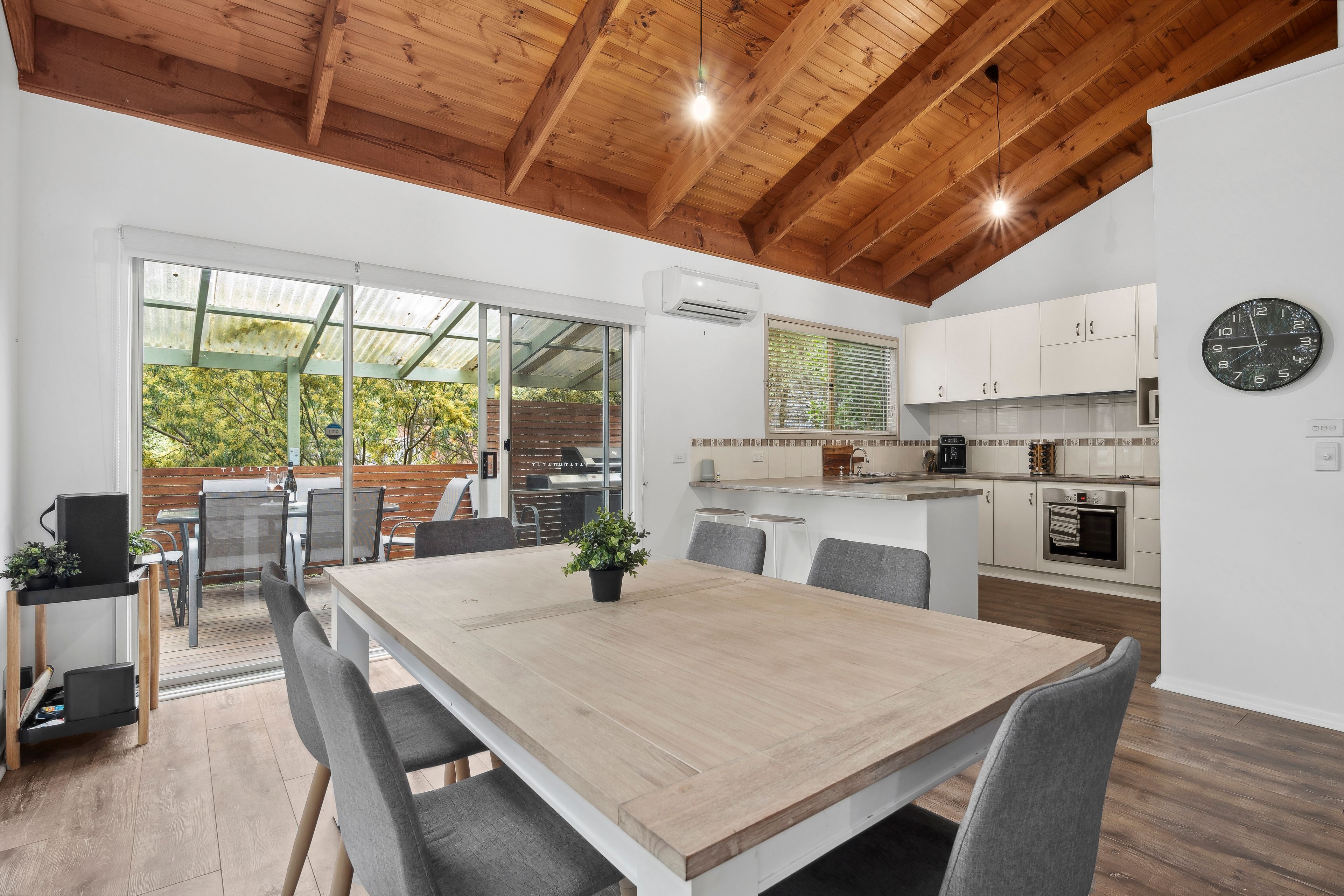 A modern kitchen with white cabinets, a black clock, and a wooden ceiling.