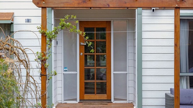 A wooden pergola entrance to a house with a glass door and a small porch area. - Walk2Everything (Anglesea)