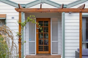 A wooden pergola entrance to a house with a glass door and a small porch area.
