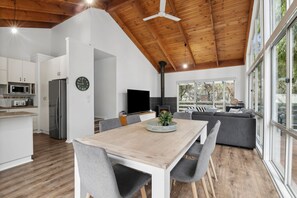 A modern kitchen with a dining area, a large window, and a built-in fireplace. - Walk2Everything (Anglesea)