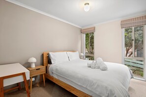A bedroom with a bed, bedside table, lamp, and a view of greenery through the window.