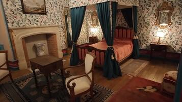 Een klassieke slaapkamer met een hemelbed, een open haard, een kroonluchter en behang met een patroon.