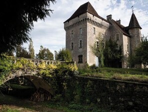 Um edifício histórico de pedra com uma torre imponente e uma ponte em primeiro plano.