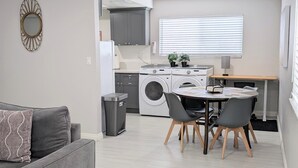 Moderni asunto, jossa on harmaa sohva, ruokapöytä tuoleineen, pesukone ja pieni roskakori.