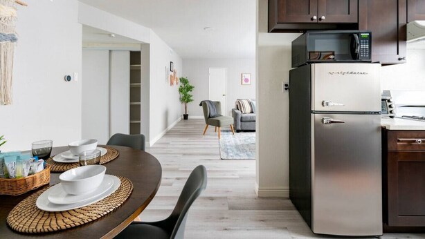 A modern kitchen with a stainless steel refrigerator, a microwave, and a built-in oven. There is a dining area with a wooden table and chairs, and a kitchen counter with a microwave above it. - DT Alhambra 2Br/2Ba with King bed + EV Charger (Alhambra)