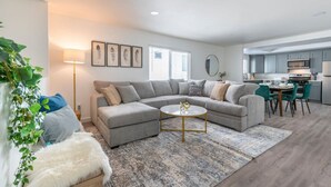 Ein modernes Wohnzimmer mit einem Ecksofa, einem runden Couchtisch und einem Essbereich mit Tisch und Stühlen.