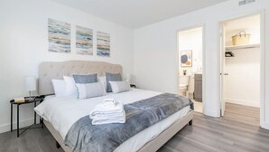 Una camera da letto moderna con un letto grande, un comodino e un tavolino. Sopra il letto, tre opere d'arte appese al muro.