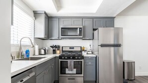 Una cucina moderna con mobili grigi, un frigorifero in acciaio inossidabile, un forno a microonde, un piano cottura e una lavastoviglie.
