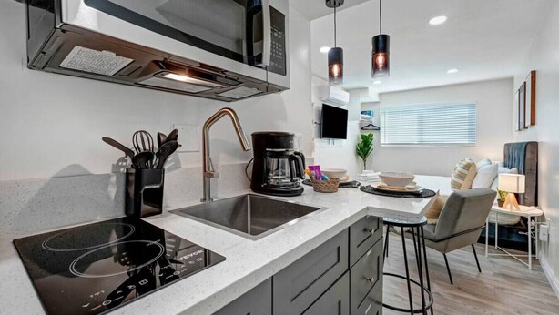 Una cocina moderna con horno empotrado, microondas y cafetera. Hay una zona de comedor con mesa y sillas.