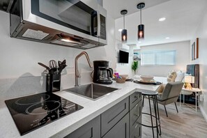 A modern kitchen with a built-in stove, a microwave, and a coffee maker. There is a dining area with a table and chairs.