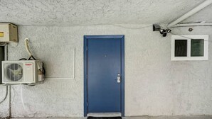 Una puerta azul con cerradura de seguridad, una unidad de aire acondicionado y una ventana a la derecha.