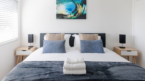 A neatly made bed with a dark blanket, two pillows, and a folded towel. There is a wall-mounted artwork above the bed.