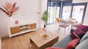 Ein modernes Wohnzimmer mit einem Holztisch, einer roten Sofakissen, einer weißen TV-Konsole und einem Essbereich mit Tisch und Stühlen.