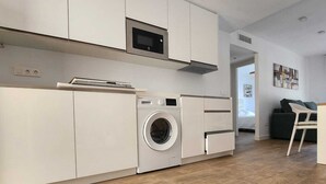 Eine moderne Küche mit weißen Schränken, einer eingebauten Mikrowelle, einer Waschmaschine und einem Essbereich mit Tisch und Stühlen.