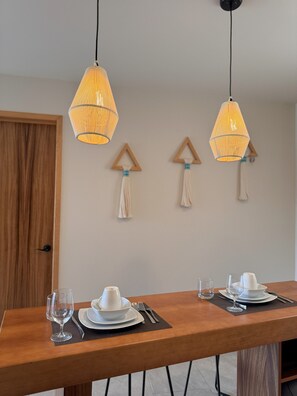 Ein Essbereich mit einem Holztisch, gedeckt für zwei Personen, zwei hängenden Pendelleuchten und zwei Wanddekorationen.