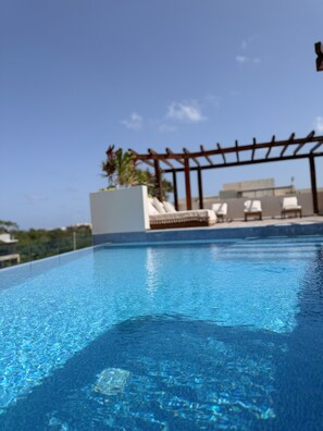 Ein klares, blaues Schwimmbecken mit einer Pergola und Liegestühlen.