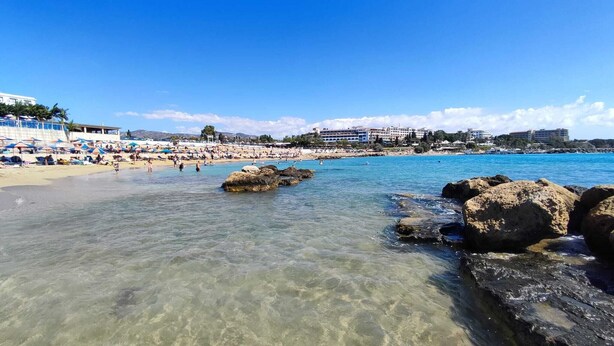 Una playa con agua cristalina, rocas y sombrillas.