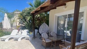 Un patio al aire libre con sillones de descanso, una mesa y sillas de mimbre.