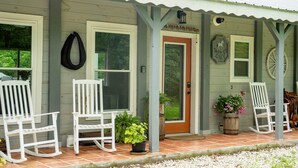 Eine Veranda mit weißen Schaukelstühlen, einer Holztür und einem Schild mit der Aufschrift 'Dappled Grey'.