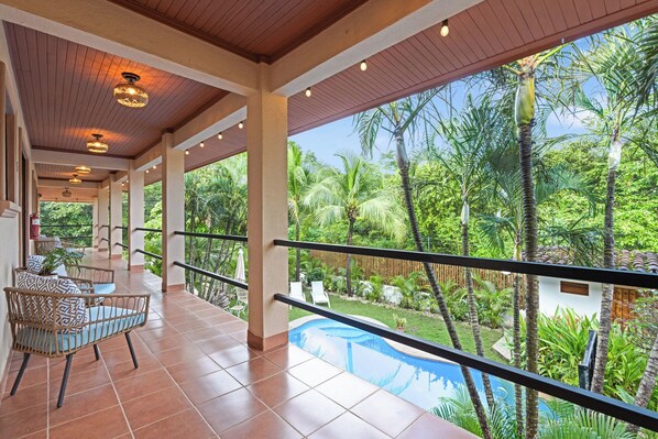 A covered outdoor area with a pool, chairs, and a view of a lush garden. - Villas Vibras (Tamarindo)