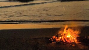 Escena de playa con una fogata al atardecer.