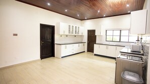 A spacious kitchen with white cabinets, a wooden ceiling, and a window providing natural light. - LC Lodge & Event Centre (Kumasi)