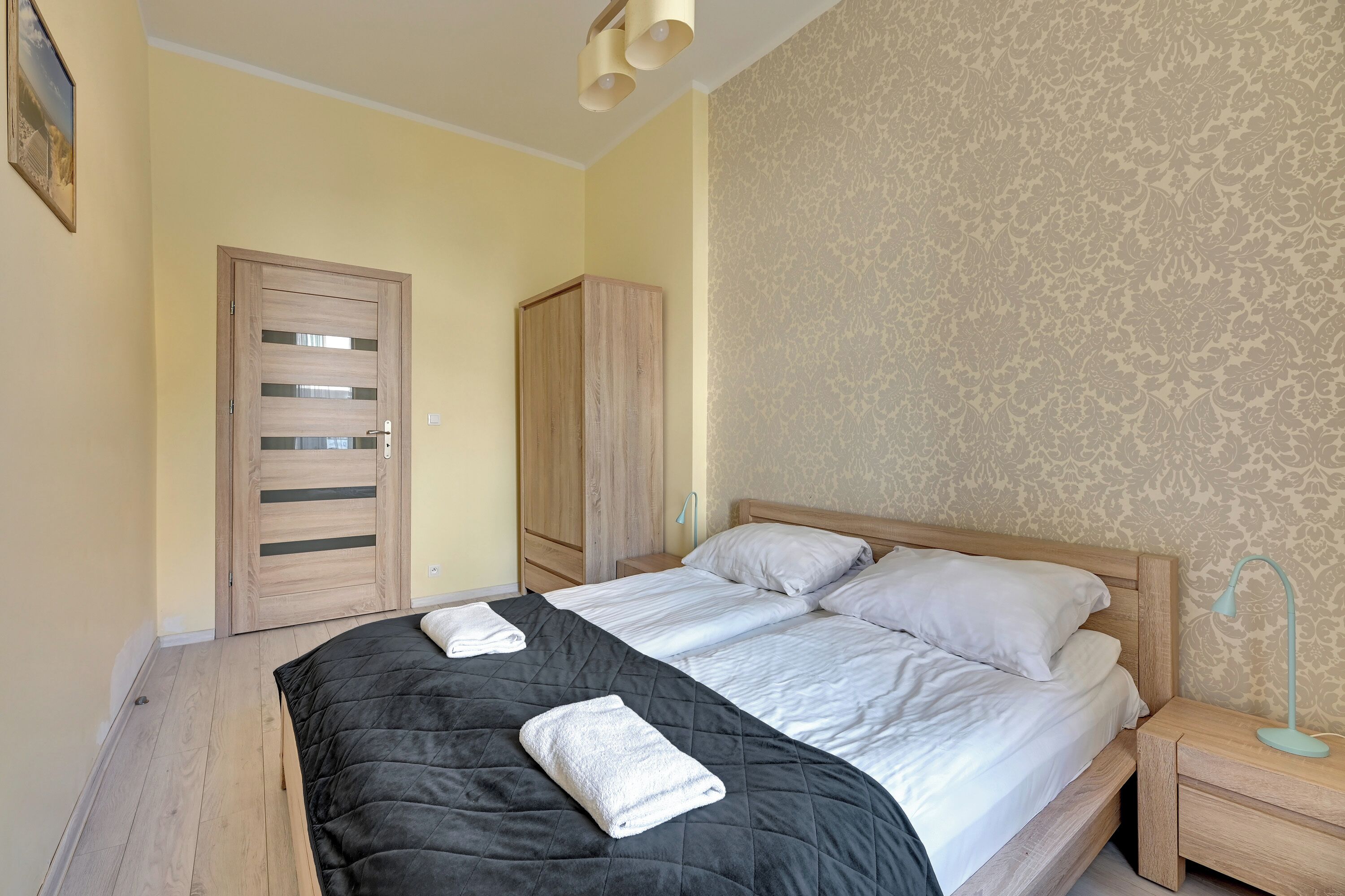 A bedroom with a large bed, two nightstands, a wardrobe, and a door.
