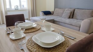 A dining table set with plates, glasses, and cutlery, a woven placemat, and a sofa in the background. - Bryza by Grand Apartments (Sopot)