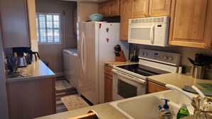 A compact kitchen with wooden cabinets, a refrigerator, a microwave, an oven, and a sink. - Direct Beachfront Sea Oats Condo in Cocoa Beach (Cocoa Beach)