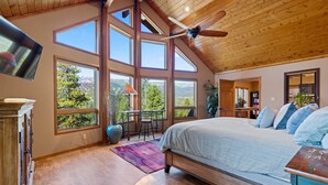 Une chambre spacieuse avec un grand lit, un ventilateur de plafond et de nombreuses fenêtres donnant sur l’extérieur.