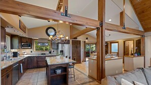 Une cuisine spacieuse dotée d’un grand îlot central, de poutres en bois et offrant une vue sur l’extérieur.
