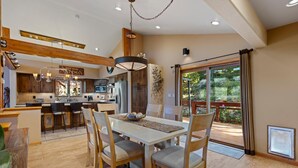Une cuisine moderne avec des meubles en bois, un coin repas doté d’une grande table et de chaises, et une vue sur une terrasse accessible par une porte vitrée.