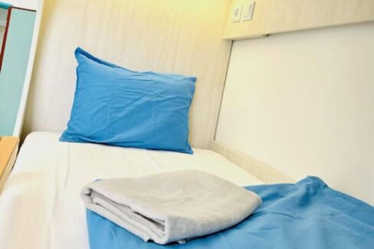 A small, neatly made bed with a blue pillow and a folded white blanket.