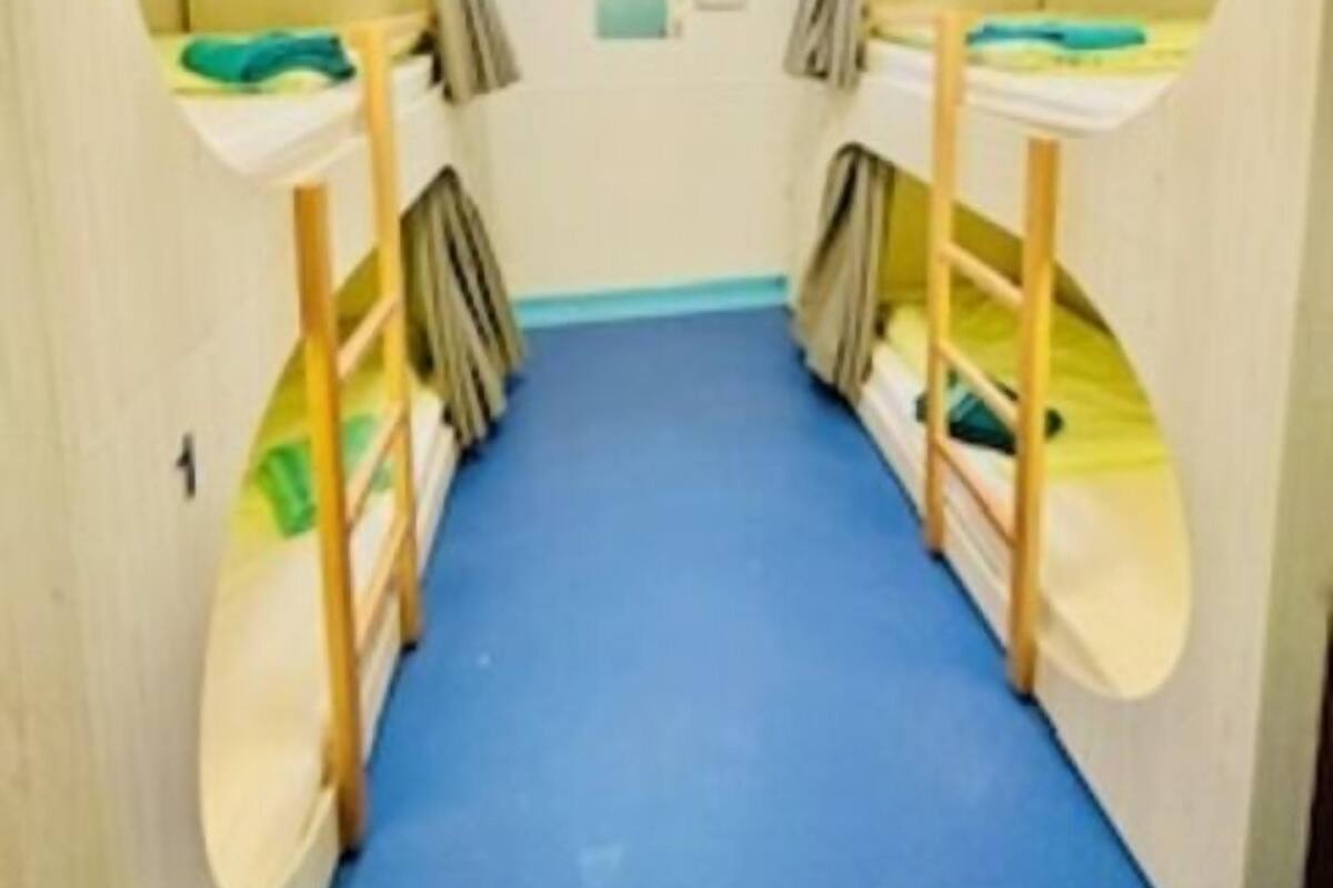 A narrow corridor with bunk beds on either side, a small window at the end, and a blue carpet.