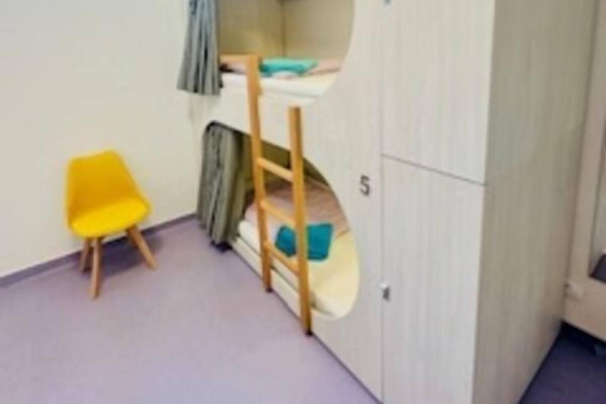 A room with a bunk bed, a small yellow chair, and a window.