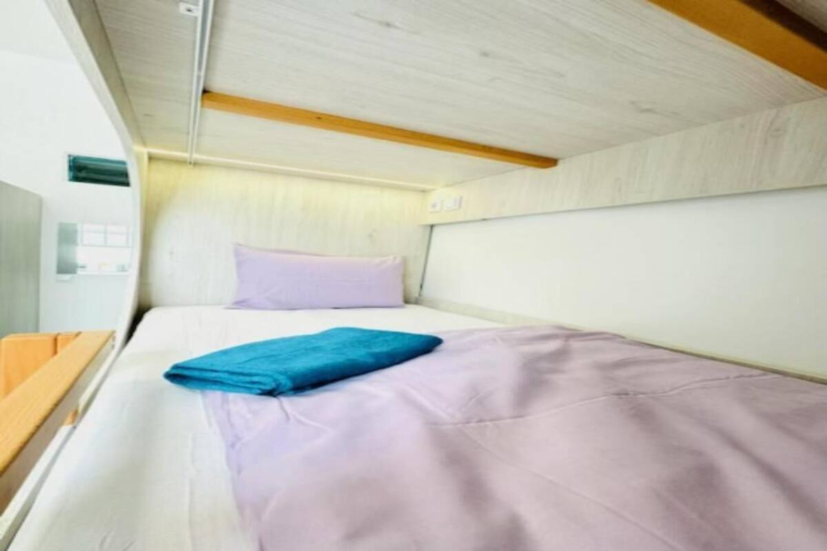 A compact, modern room with a single bed, a wooden headboard, and a small bedside table.