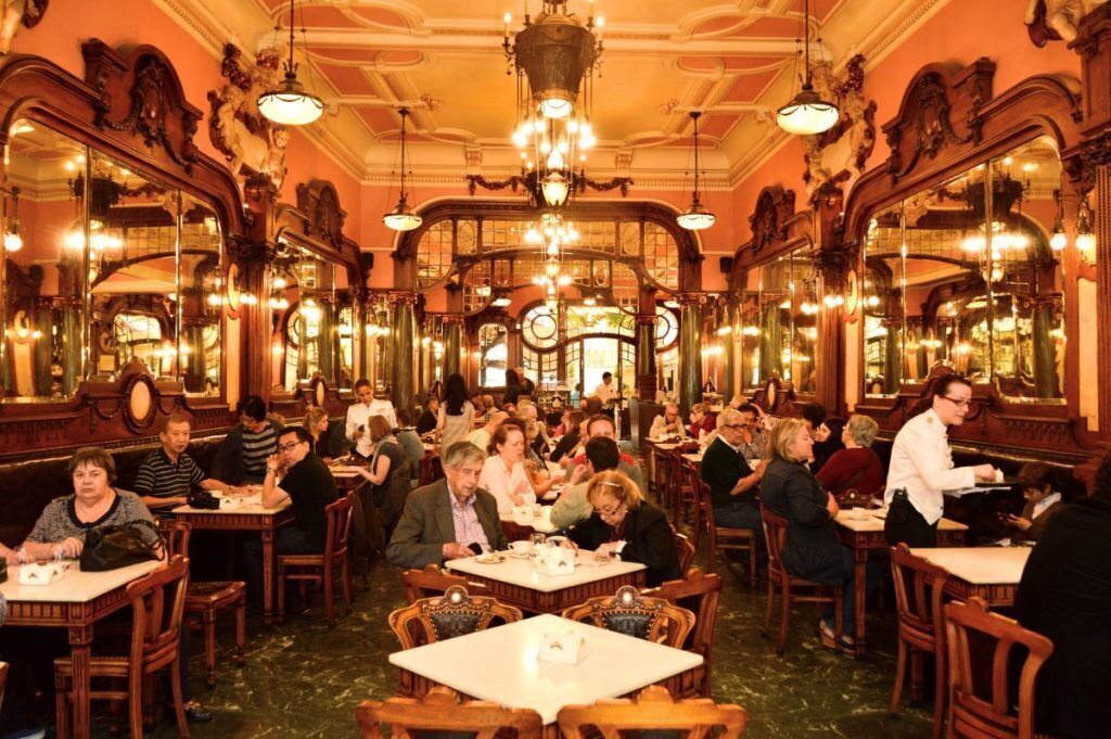 A crowded restaurant with ornate decor and chandeliers.