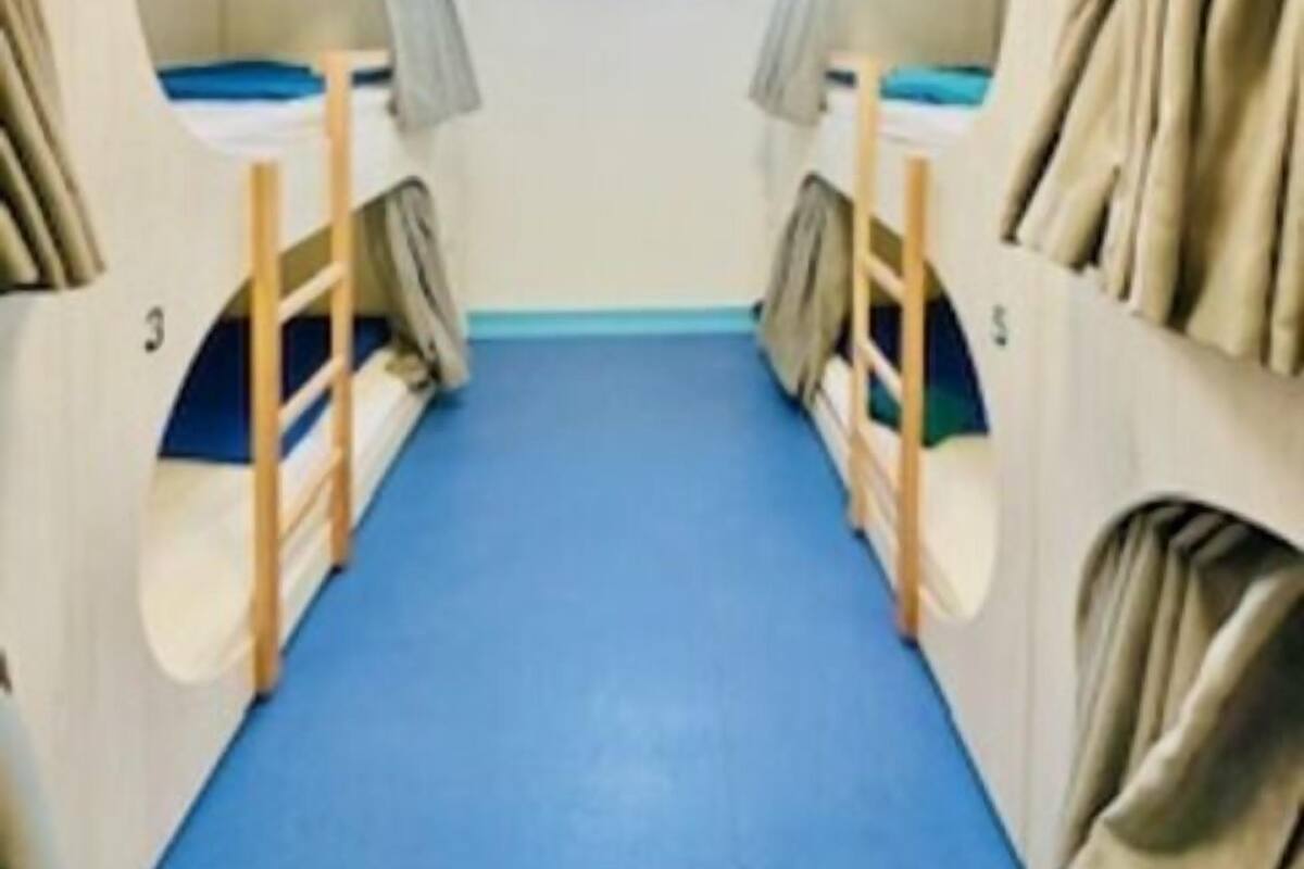 A narrow corridor with bunk beds on either side, a blue carpet, and a skylight at the end.