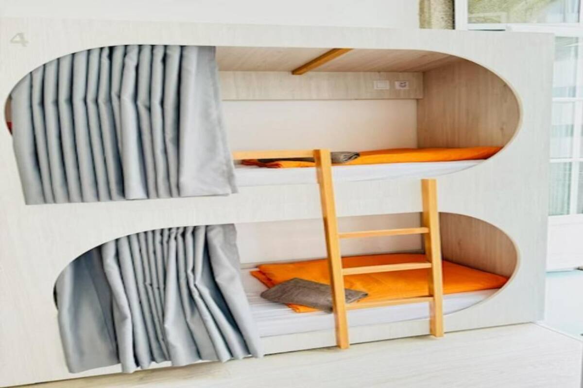 A bunk bed with a ladder, grey curtains, and orange bedding.