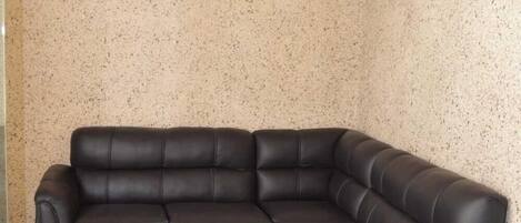 Un sofá modular en esquina en una habitación con pared beige con salpicaduras y suelo de baldosas blancas.
