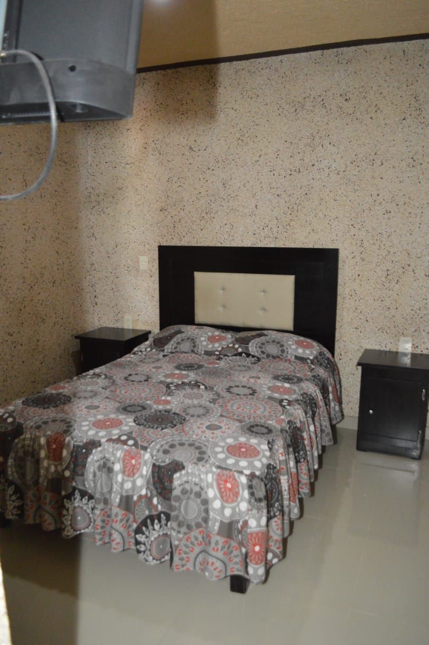 A bedroom with a bed, two nightstands, a headboard, and a wall-mounted TV.